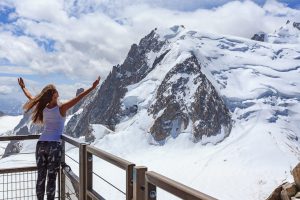 Girl with arms raised facing snowy mountain